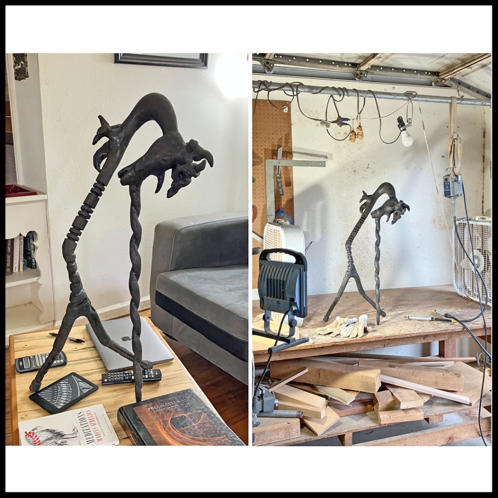 Rustic wood sculpture of dark, bent unicorn, facing downwards with spiraled main horn askew and acting as support. www.SawdustRiver.com