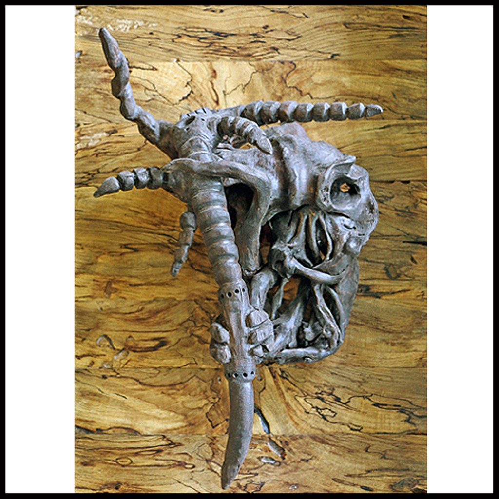 This intricate wood-carved mask presents a grotesque visage with spiraling horns and claws that twist outward. Hollow eyes peer out from a knotted face that seems to be unraveling. Wild and primal. www.SawdustRiver.com